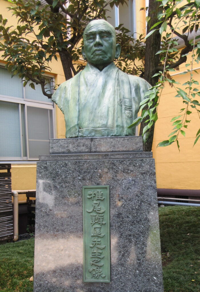 モダンな旧校舎を背景にした椎尾弁匡第6、9、14代学長像